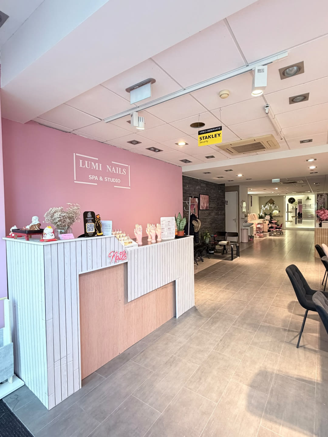 Receptie van Lumi Nails Studio & Spa met het bord Lumi Nails Spa & Studio, houten toonbank en roze muur