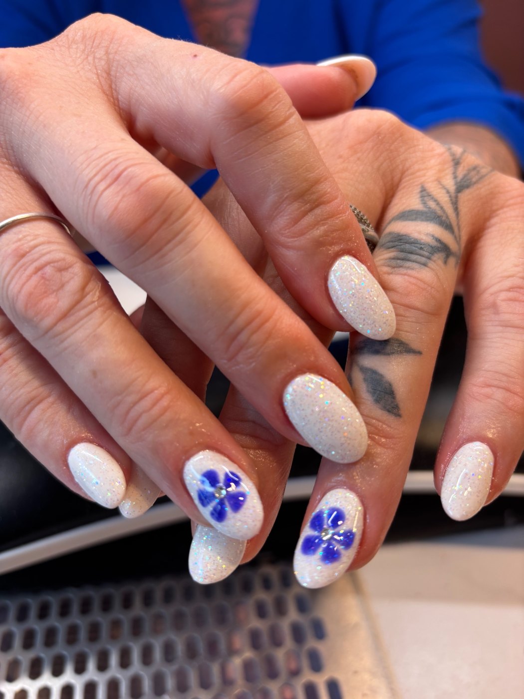 Korte nagels met iriserende witte glitter en blauwe bloemen